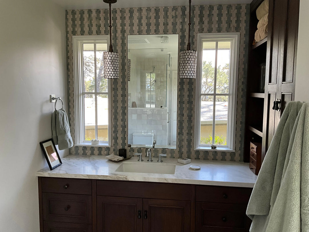 Geometric mosaic tile backsplash behind a bathroom vanity with marble countertop, dark wood cabinets, and pendant lighting.